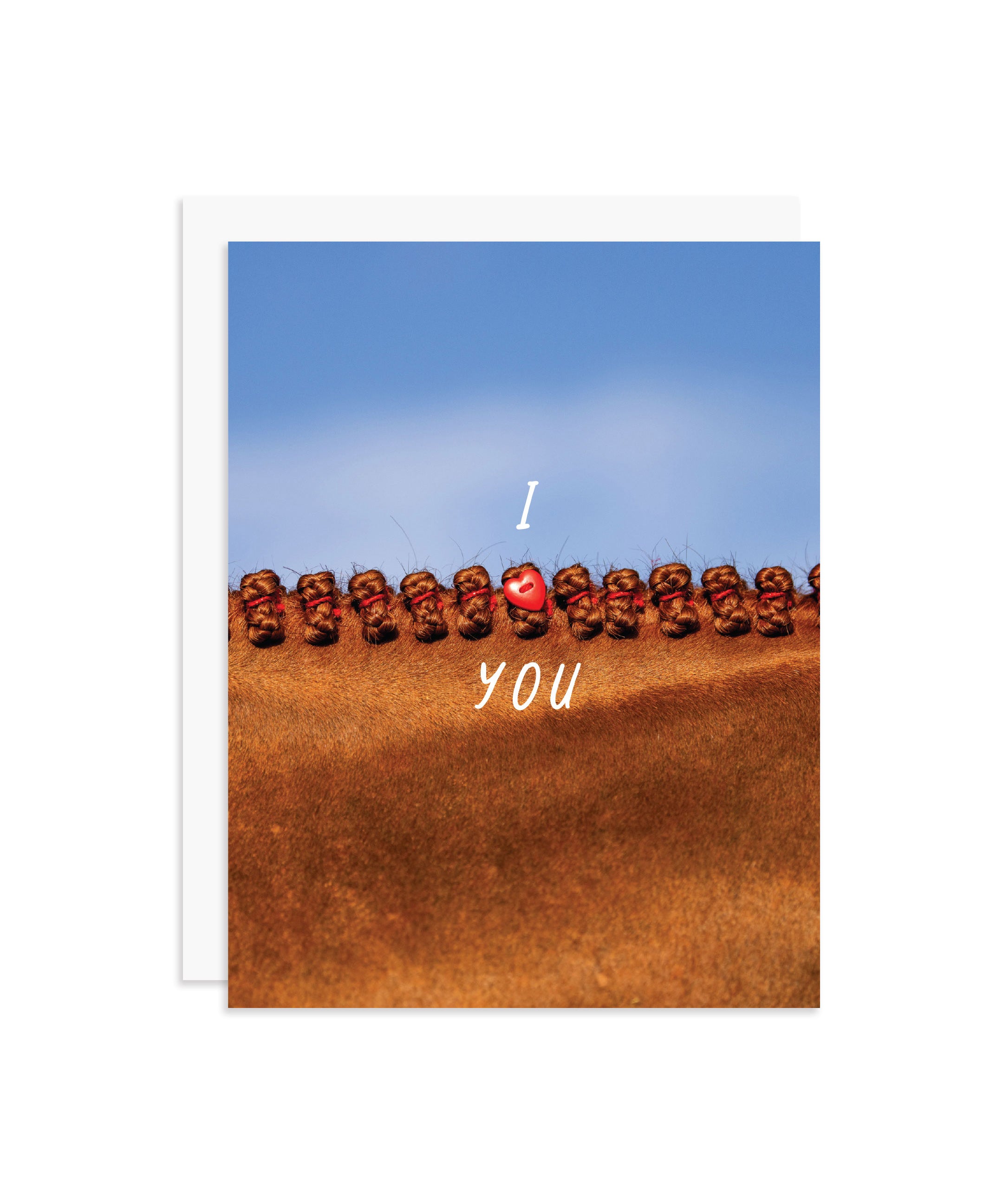 A greeting card featuring a close-up photograph of a chestnut horse's braided mane under a blue sky, with the words 'I' and 'YOU' and a red heart charm in the center. A white envelope is partially visible behind the card on a white background.