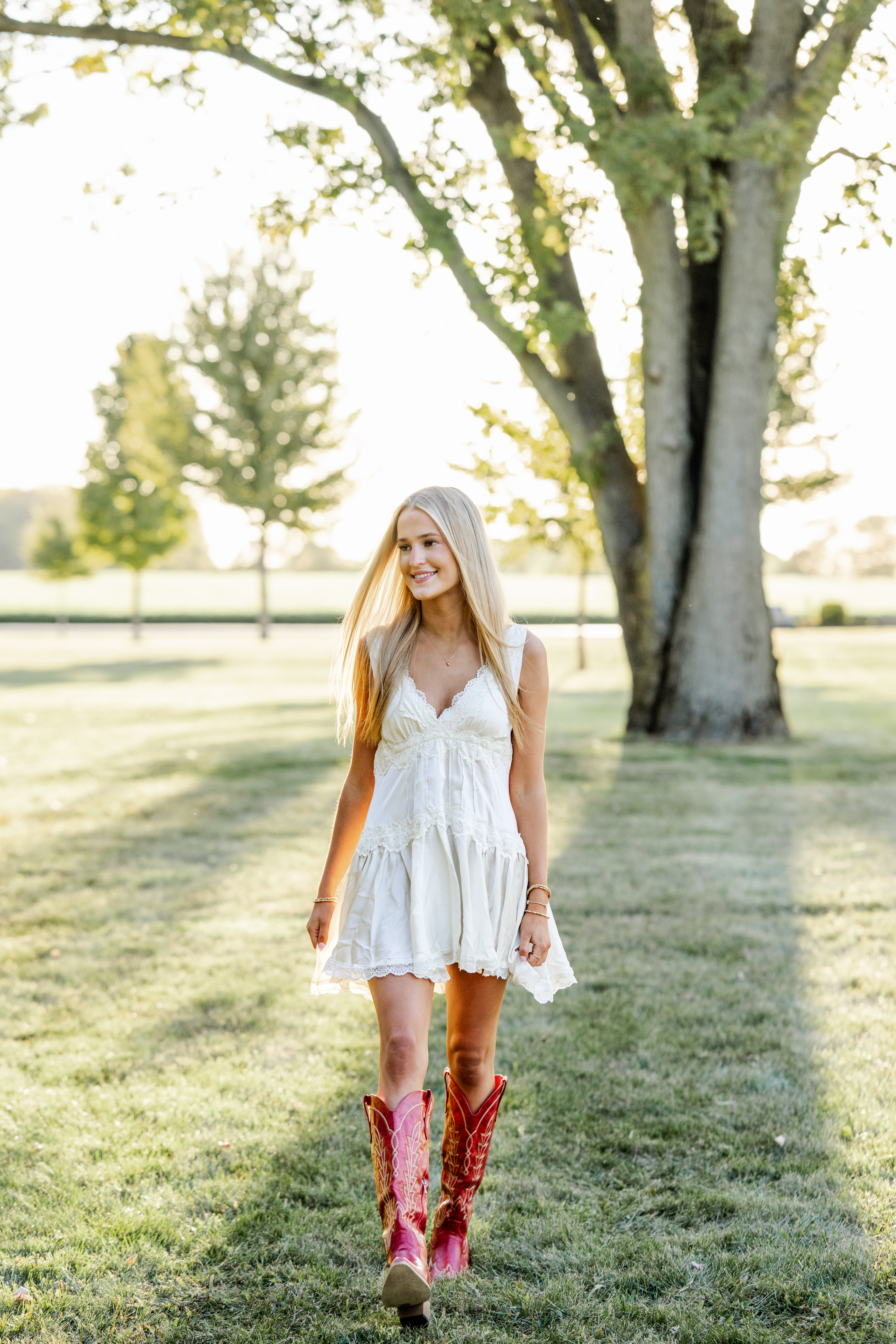 Candid moment of teen girl walking through sunlit field during senior photo session in Sheridan, Indiana.